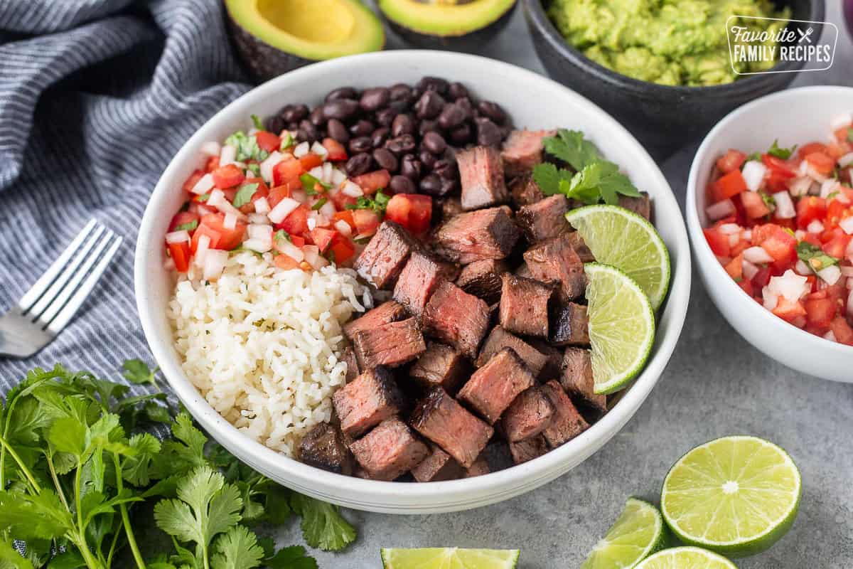 Bowl of Chipotle steak with rice, black beans, pico, lime wedges and cilantro.