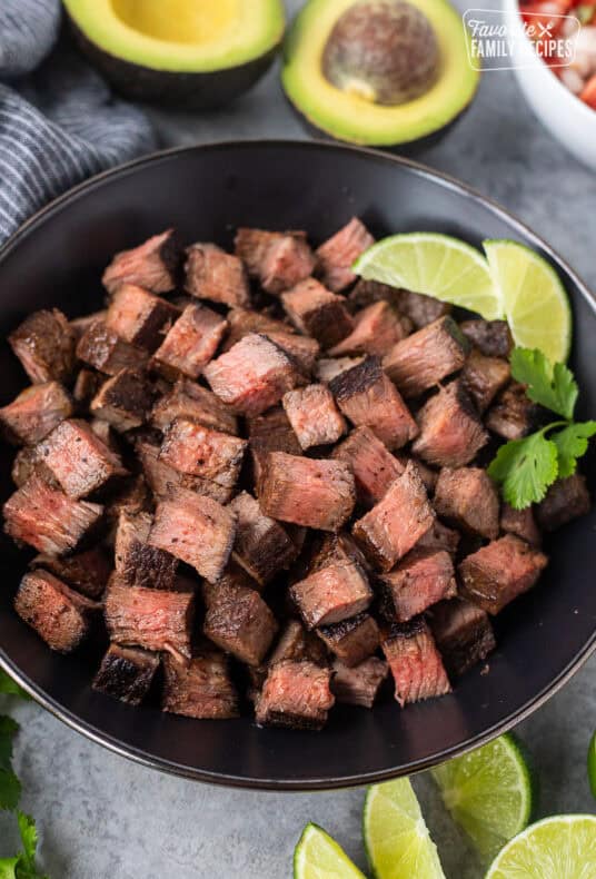 Bowl of Chipotle steak with lime wedges and cilantro on the side.