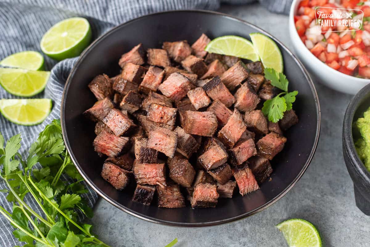 Bowl of Chipotle steak with lime wedges and cilantro on the side.