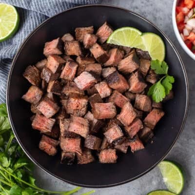 Bowl of Chipotle steak with lime wedges and cilantro on the side.