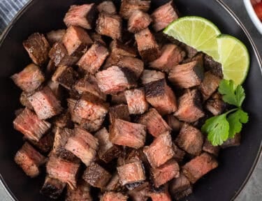 Bowl of Chipotle steak with lime wedges and cilantro on the side.