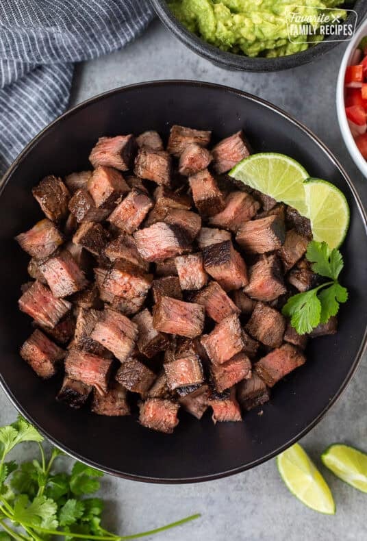 Bowl of Chipotle steak with lime wedges and cilantro on the side.