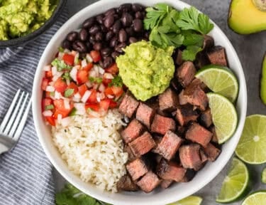 Chipotle steak with rice, black beans, pico, guacamole, lime wedges and cilantro.