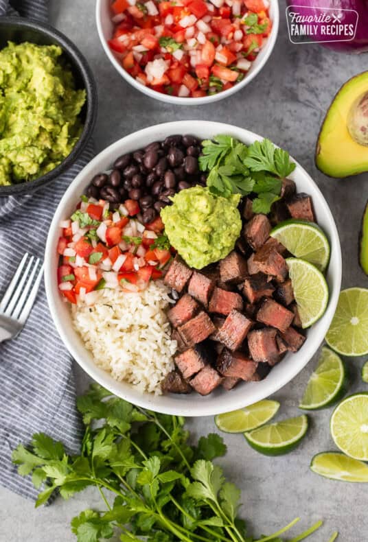 Chipotle steak with rice, black beans, pico, guacamole, lime wedges and cilantro.