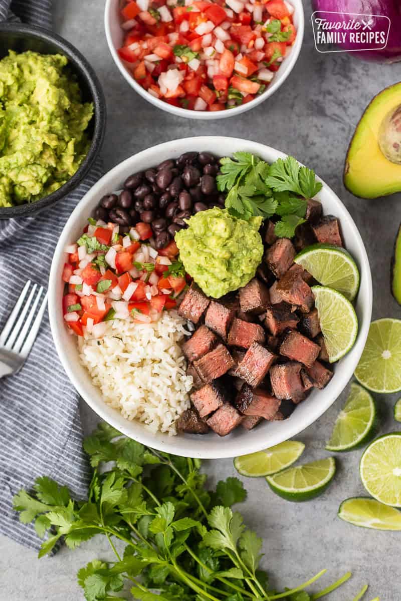Chipotle steak with rice, black beans, pico, guacamole, lime wedges and cilantro.