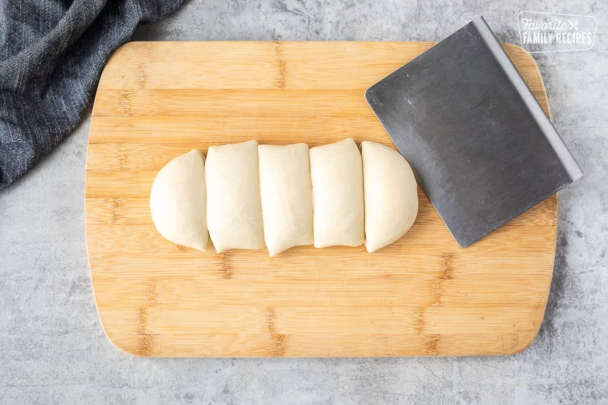 Cutting board with thawed white bread dough sectioned into five pieces.