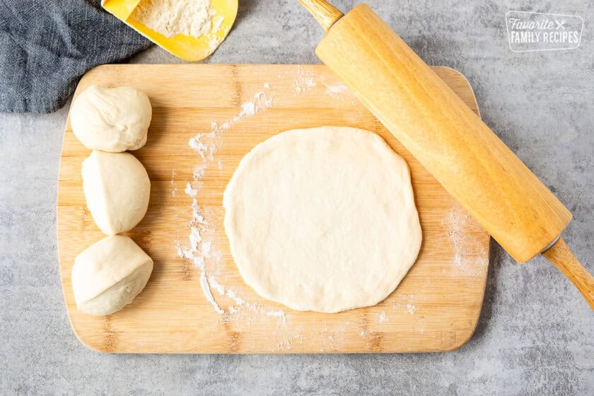 Rolled out pizza dough in round on a cutting board with a rolling pin.