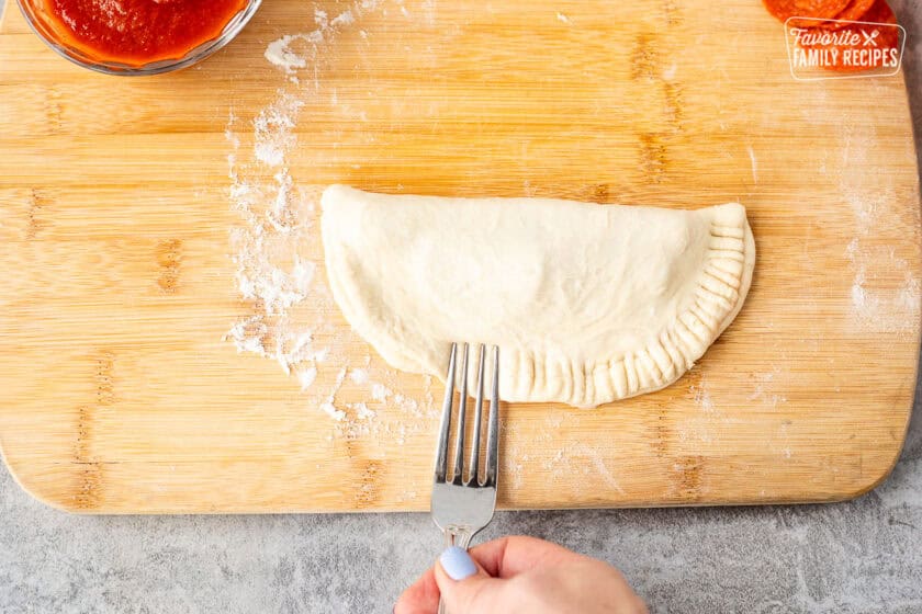 Pressing edges of calzone dough with a fork.