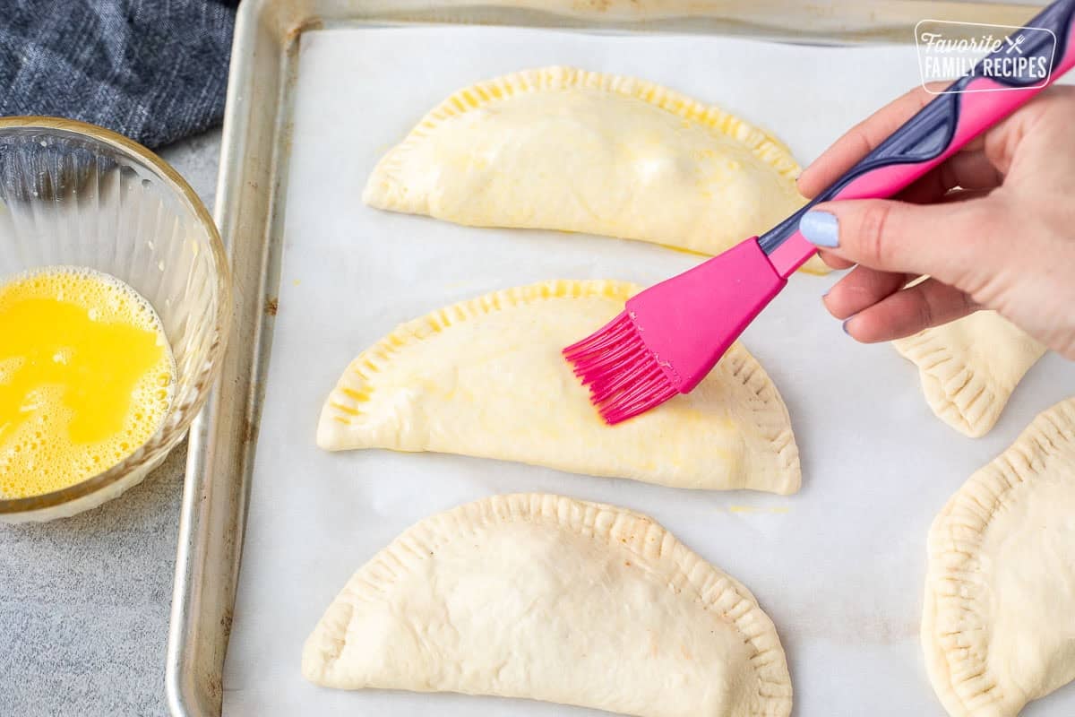 Brushing egg wash on top of calzones.