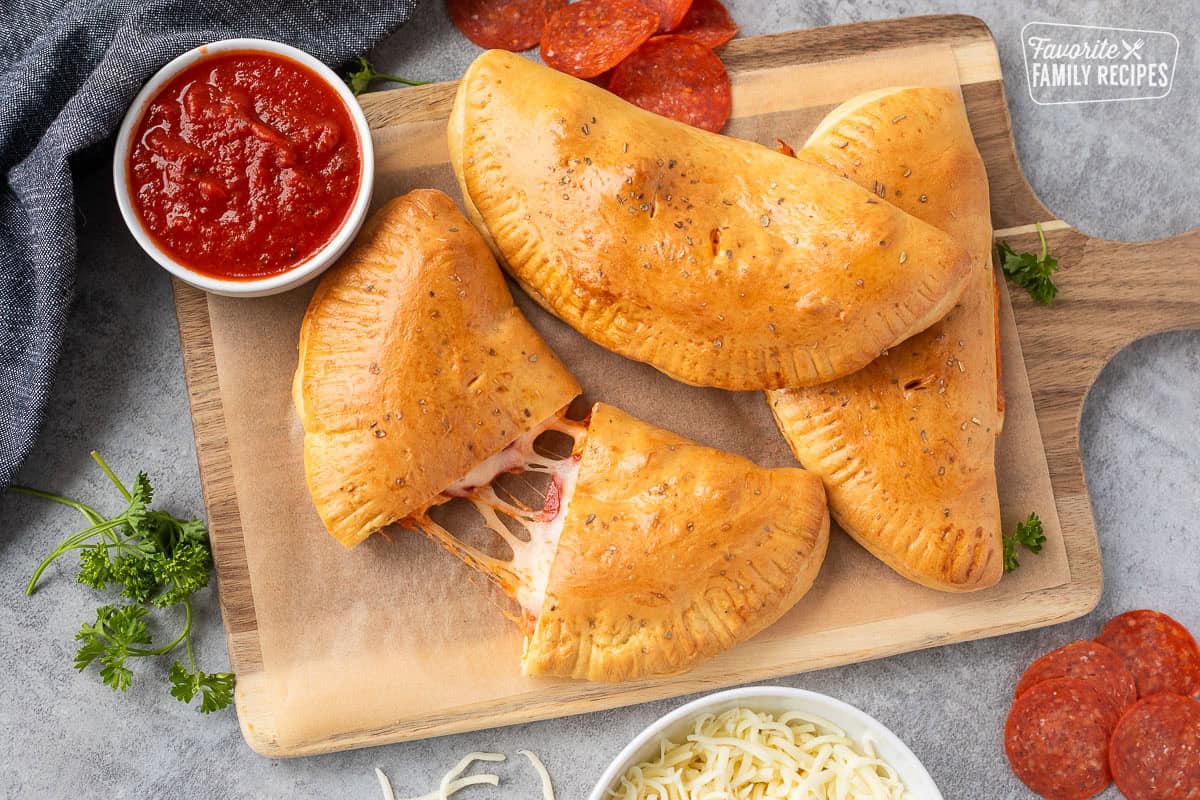Easy Calzone recipe cut in half with cheese stretching out on a cutting board. Small bowl of marinara sauce on the side.