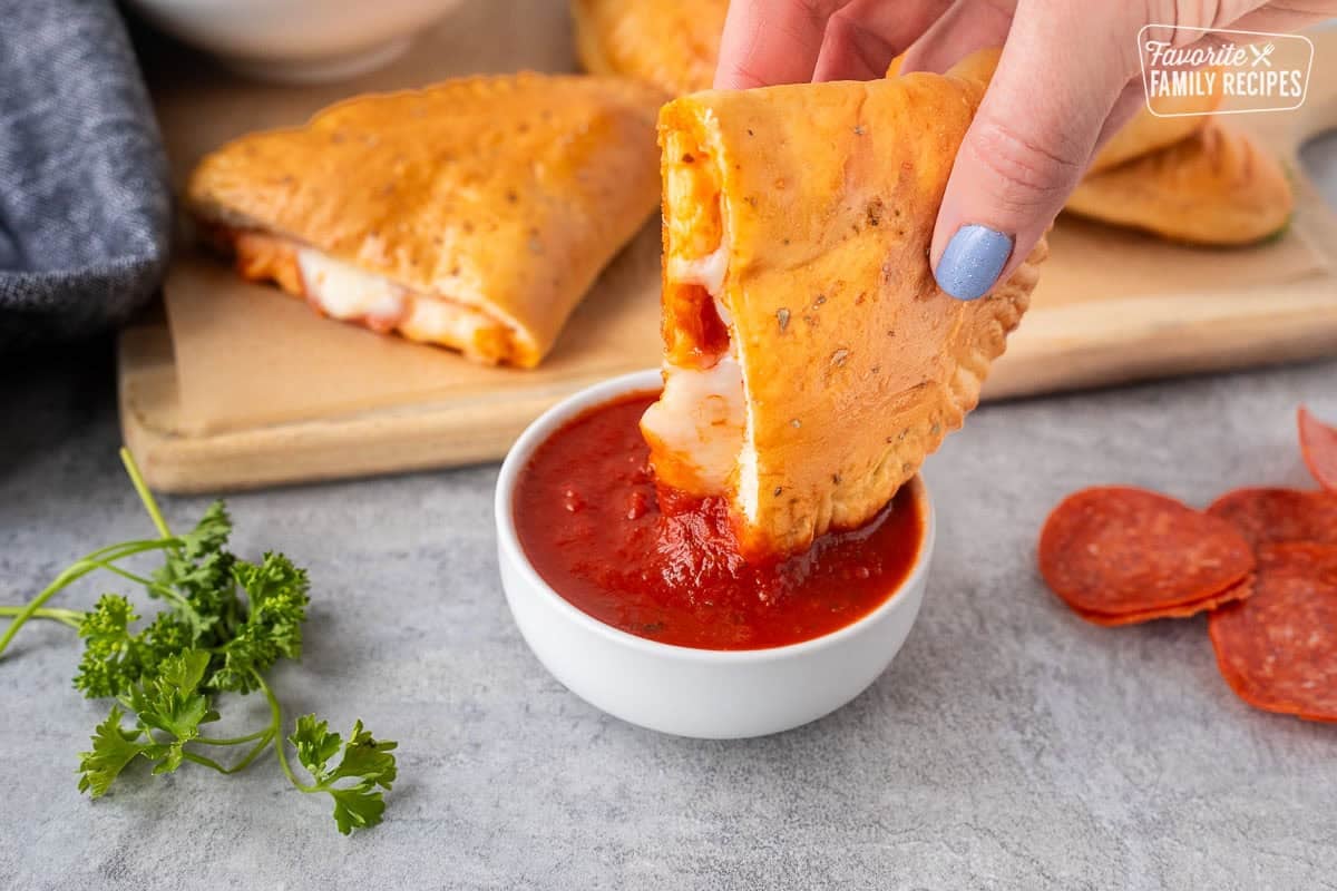 Dipping a pepperoni calzone into a small bowl of marinara sauce.