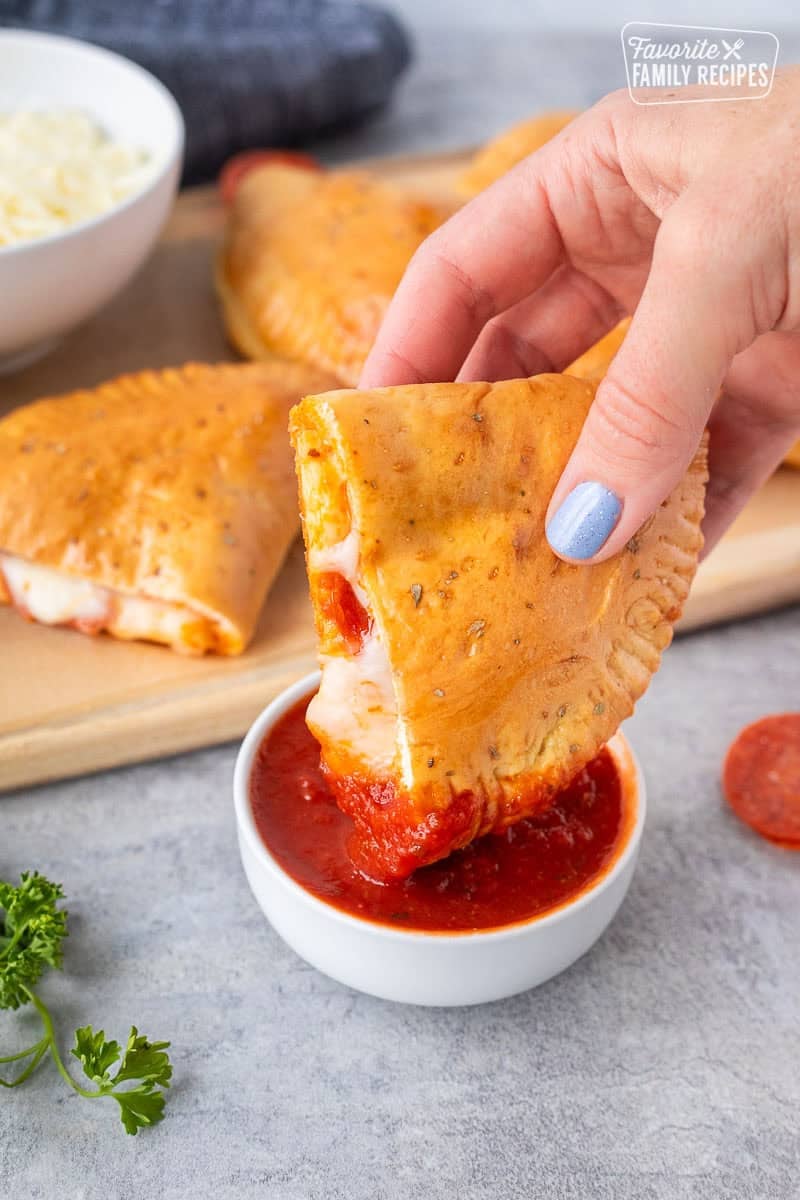 Dipping a pepperoni calzone into a small bowl of marinara sauce.