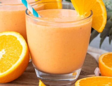 Glasses of golden detox smoothie garnished with fresh orange slices and straws.