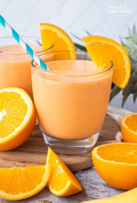 Glasses of golden detox smoothie garnished with fresh orange slices and straws.