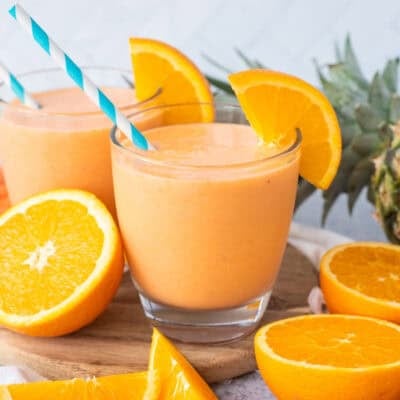 Glasses of golden detox smoothie garnished with fresh orange slices and straws.