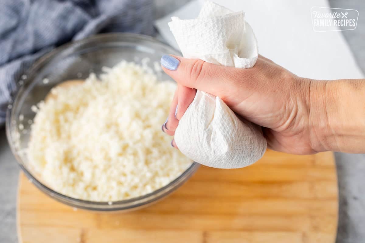 Squeezing grated cauliflower with paper towels.