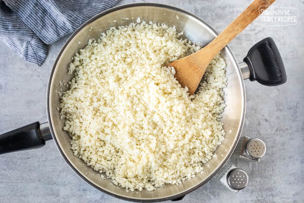 Cauliflower rice in a skillet with a wooden spoon.