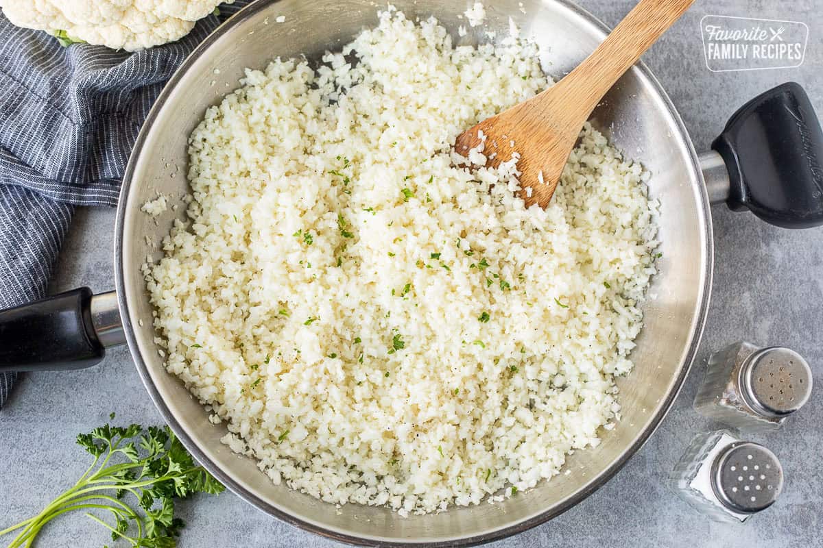 Cauliflower rice in a skillet garnished with parsley. Salt and pepper on the side.