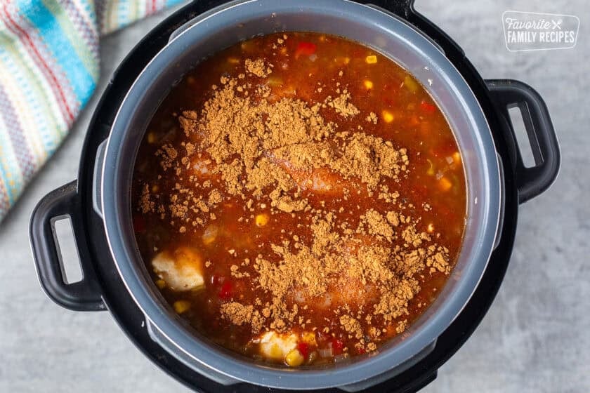 Instant pot with chicken and taco seasoning in enchilada sauce mixture.