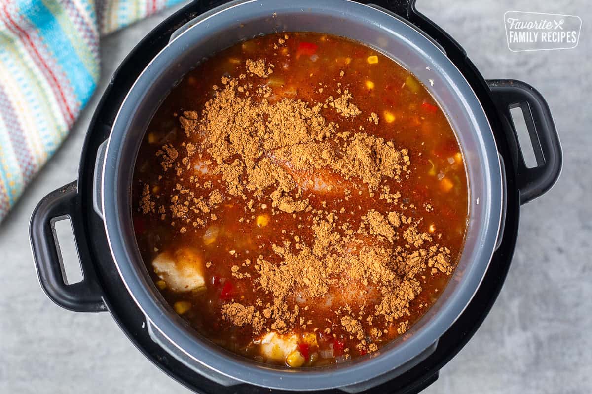 Instant pot with chicken and taco seasoning in enchilada sauce mixture.