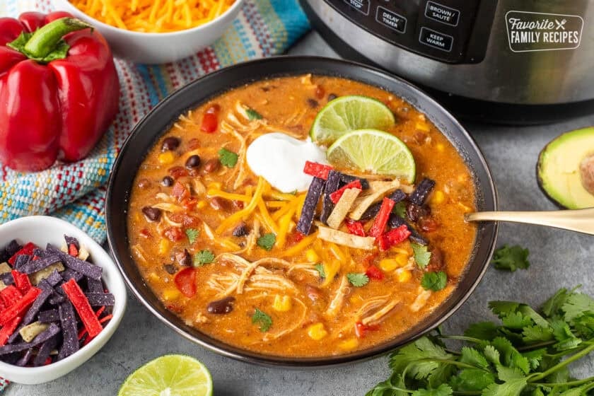 Instant pot enchilada soup in a bowl garnished with cilantro, tortilla strips, sour cream and lime wedges.