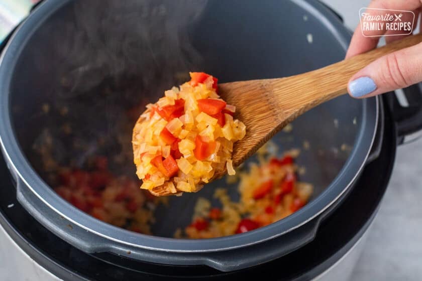 Spoon holding sautéed onions and red bell peppers.