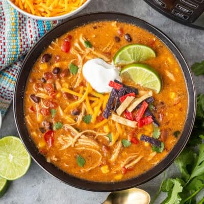 Instant pot enchilada soup in a bowl garnished with cilantro, tortilla strips, sour cream and lime wedges.