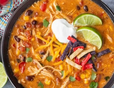 Instant pot enchilada soup in a bowl garnished with cilantro, tortilla strips, sour cream and lime wedges.