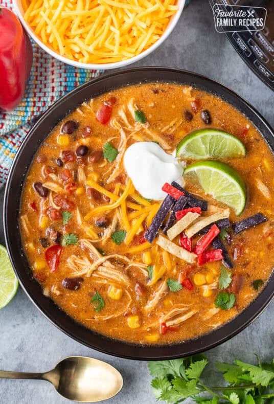 Instant pot enchilada soup in a bowl garnished with cilantro, tortilla strips, sour cream and lime wedges.