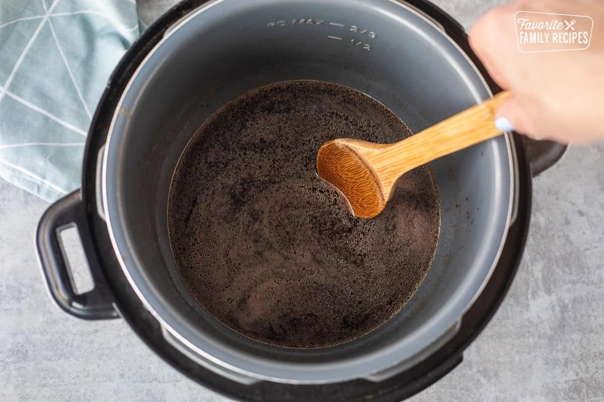 Stirring Swedish meatball broth in an instant pot with a wooden spoon.