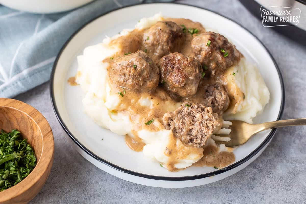 Swedish meatballs cut with fork over mashed potatoes.