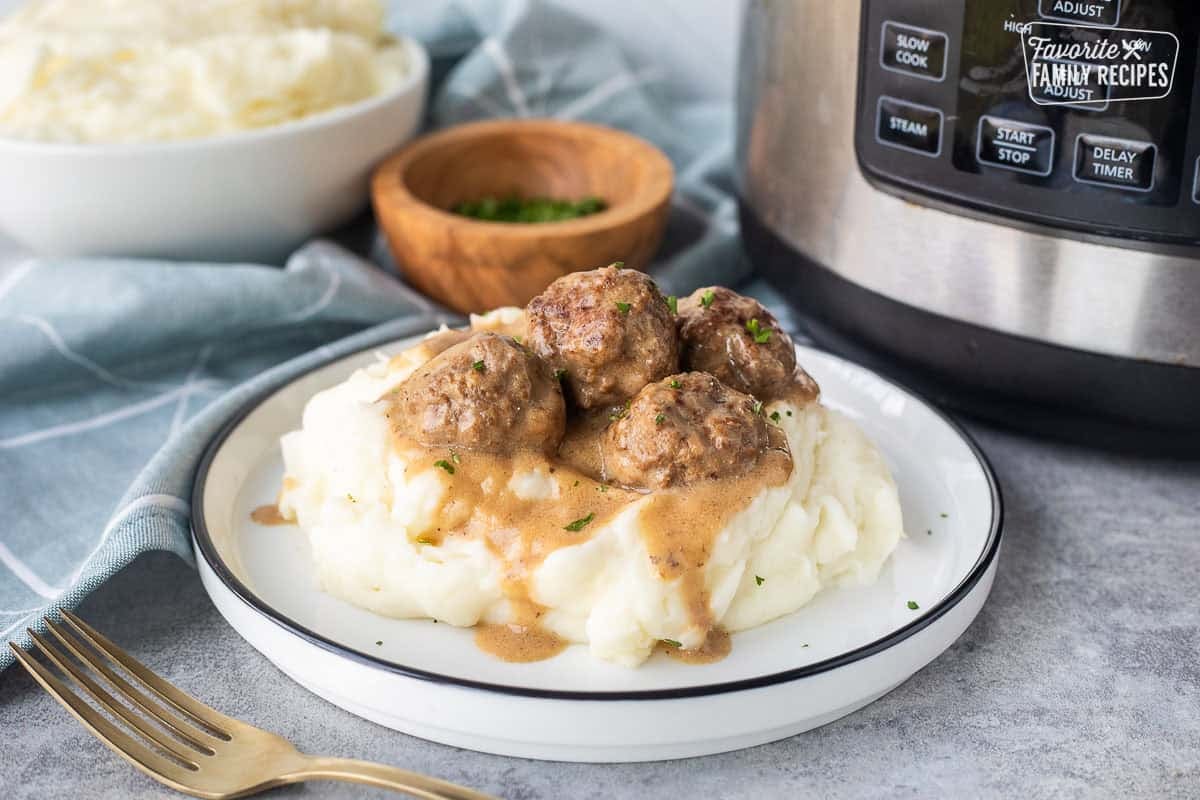 Plate of Swedish meatballs over mashed potatoes next to instant pot.
