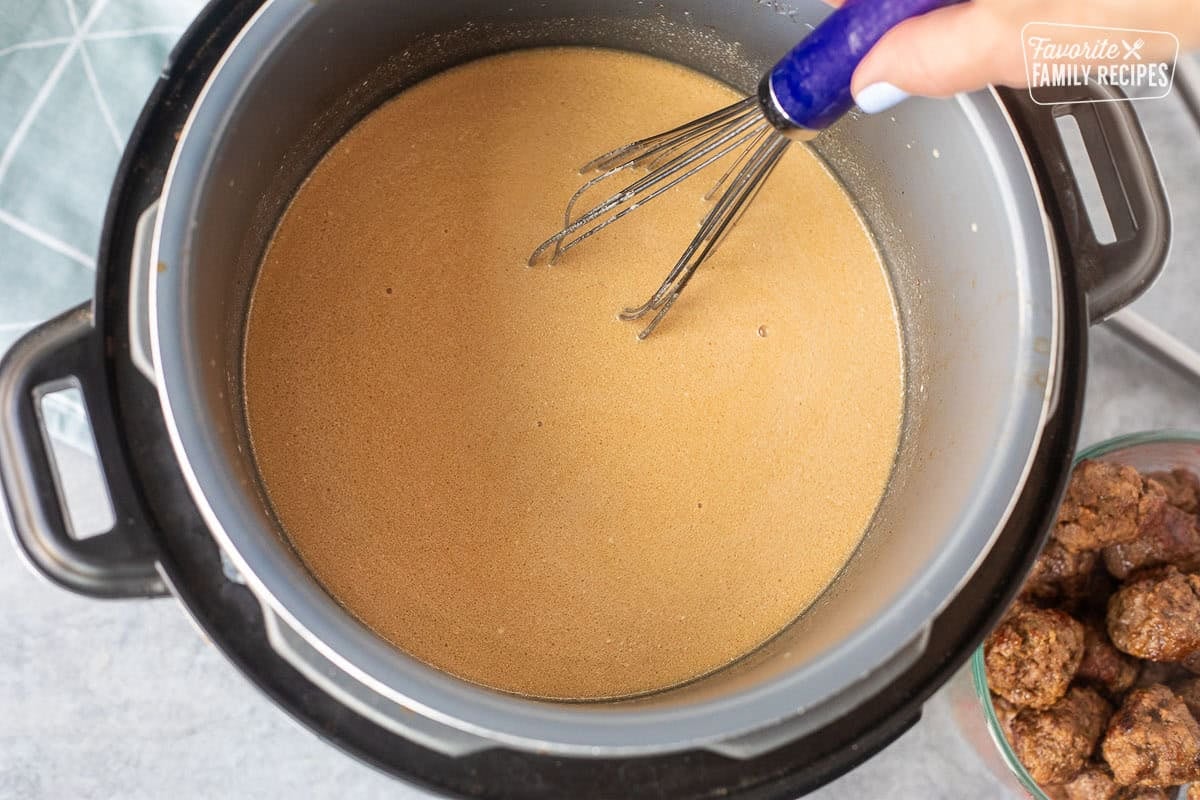 Stirring Swedish meatball broth in the instant pot with heavy cream; meatballs on the side.