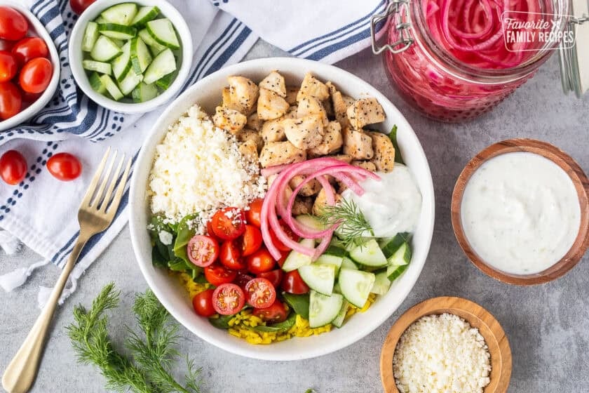 Mediterranean Bowl with rice and spinach, tomatoes, cucumbers, seasoned chicken, feta, tzatziki sauce, dill and pickled red onions.