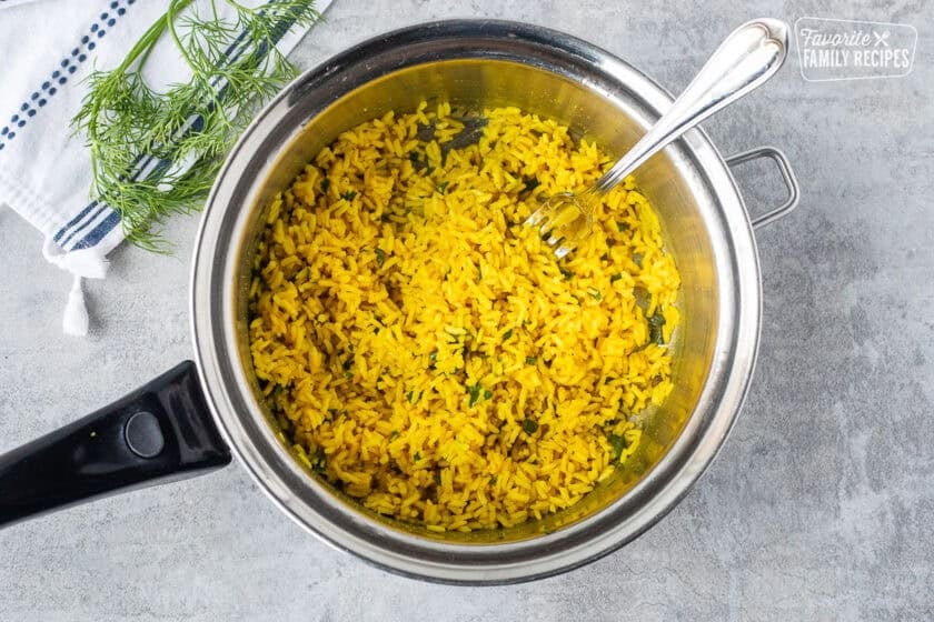 Saucepan with seasoned rice and cilantro fluffed with fork.