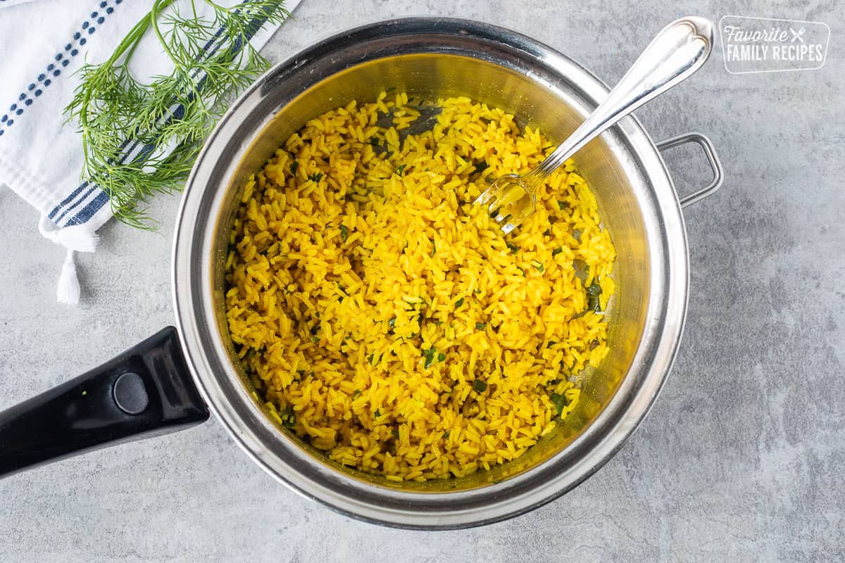 Saucepan with seasoned rice and cilantro fluffed with fork.