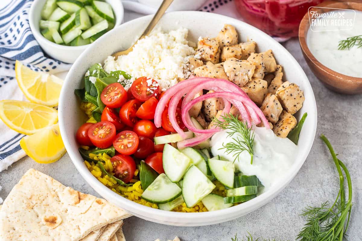 Mediterranean Bowl with rice and spinach, tomatoes, cucumbers, seasoned chicken, feta, tzatziki sauce, dill and pickled red onions.