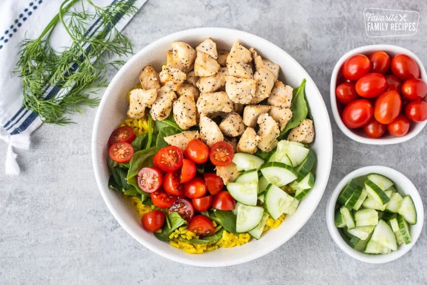 Adding chicken, tomatoes and cucumbers to Mediterranean Bowl with rice and spinach.
