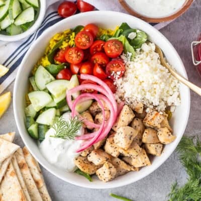 Mediterranean Bowl with rice and spinach, tomatoes, cucumbers, seasoned chicken, feta, tzatziki sauce, dill and pickled red onions.