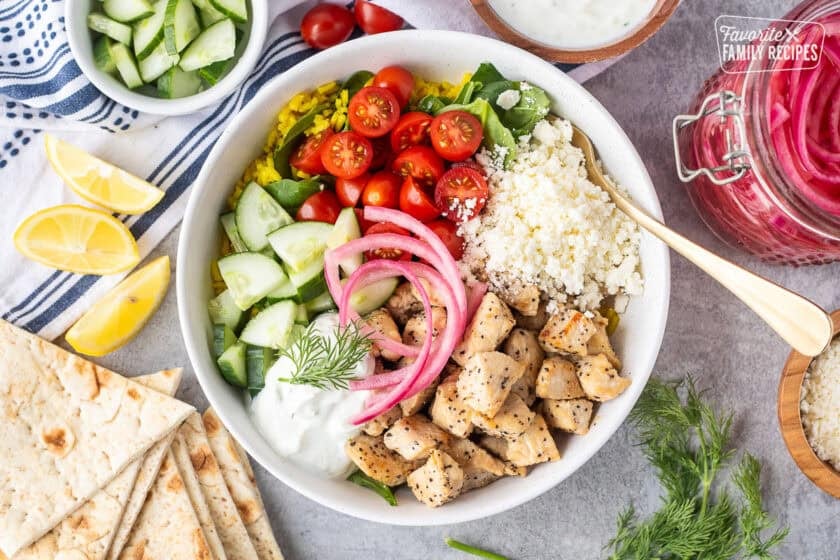 Mediterranean Bowl with rice and spinach, tomatoes, cucumbers, seasoned chicken, feta, tzatziki sauce, dill and pickled red onions.