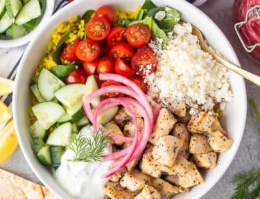 Mediterranean Bowl with rice and spinach, tomatoes, cucumbers, seasoned chicken, feta, tzatziki sauce, dill and pickled red onions.