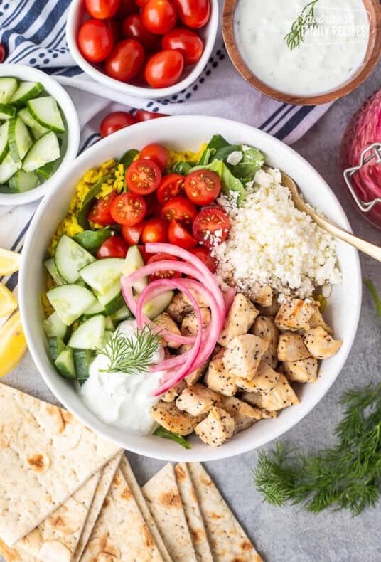 Mediterranean Bowl with rice and spinach, tomatoes, cucumbers, seasoned chicken, feta, tzatziki sauce, dill and pickled red onions.