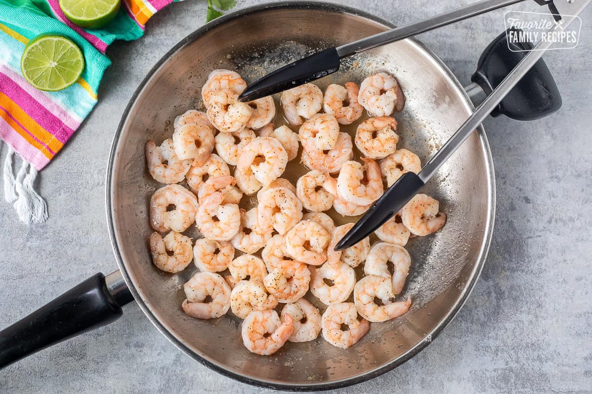 Skillet with cooked shrimp and tongs.