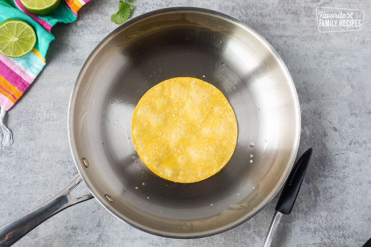 Skillet with a corn tortilla and tongs.