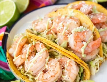 Three shrimp tacos on a plate with cabbage slaw and avocado sauce.