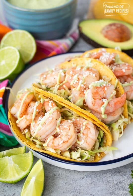 Three shrimp tacos on a plate with cabbage slaw and avocado sauce.