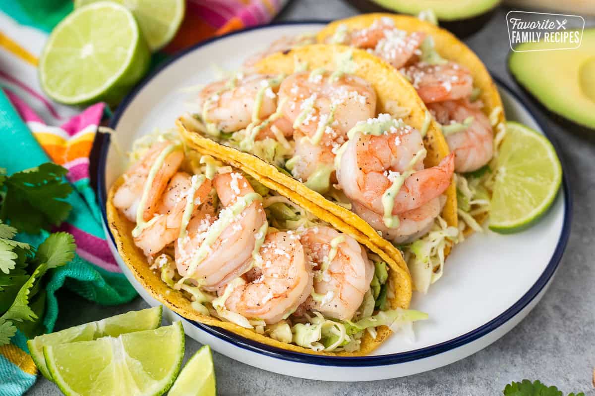 Three shrimp tacos on a plate with cabbage slaw and avocado sauce.