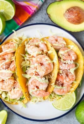 Three shrimp tacos on a plate with cabbage slaw and avocado sauce.