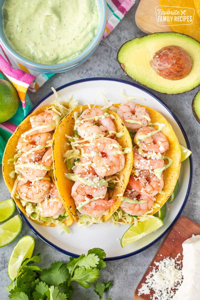 Three shrimp tacos on a plate with cabbage slaw and avocado sauce.