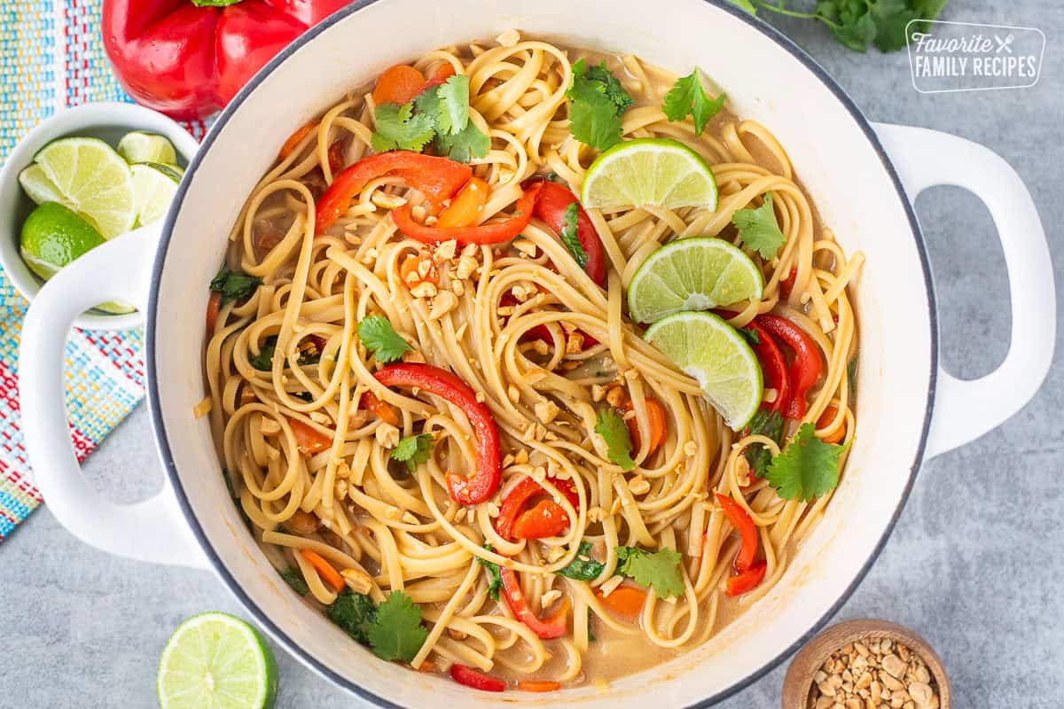 Pot of Thai Peanut Noodles garnished with fresh cilantro, peanuts and lime wedges.
